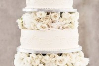 a white patterned wedding cake with white blooms between the tiers is very exquisite and chic