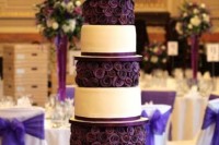a bold white wedding cake with purple ribbons and deep purple blooms between the tiers