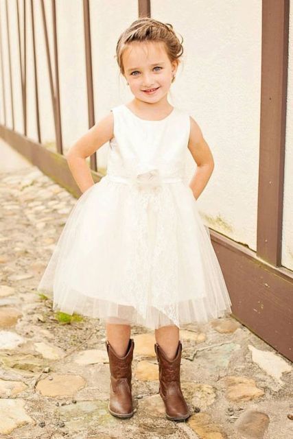 a white sleeveless dress with a plain top and a layered tulle skirt, cowboy boots and a cool braided updo