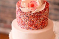 a bright wedding cake with white tiers and with a colorful sprinkle one for a contrast plus a sugar bloom