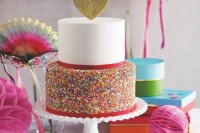 a contrasting wedding cake with a white and sprinkle tier, with red ribbons and a gold glitter heart on top