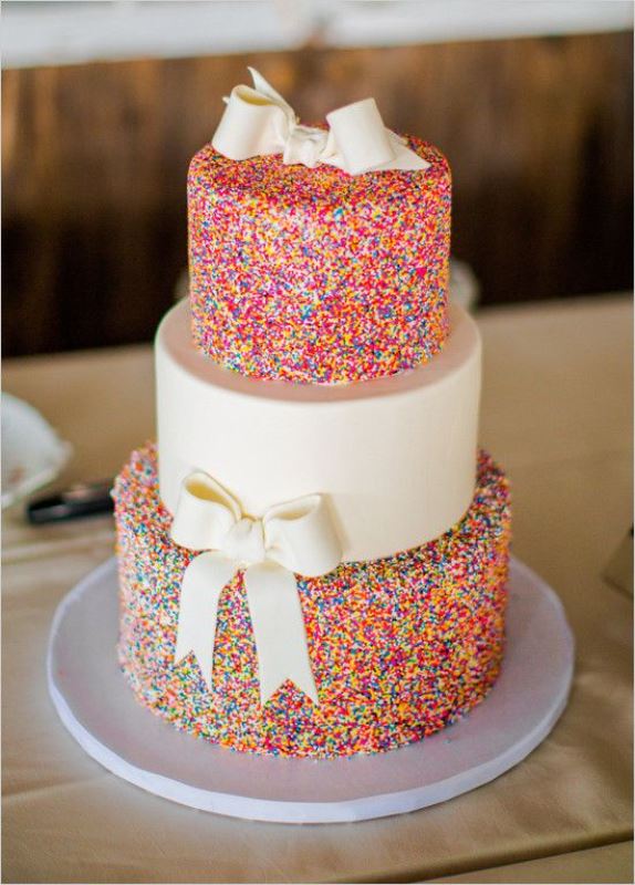 a contrasting wedding cake with sprinkle and white tiers and white sugar bows for a whimsical and bright wedding