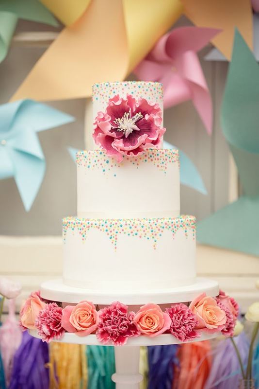 a white wedding cake with colorful sprinkles and a pink sugar bloom is a fun and bold idea to rock
