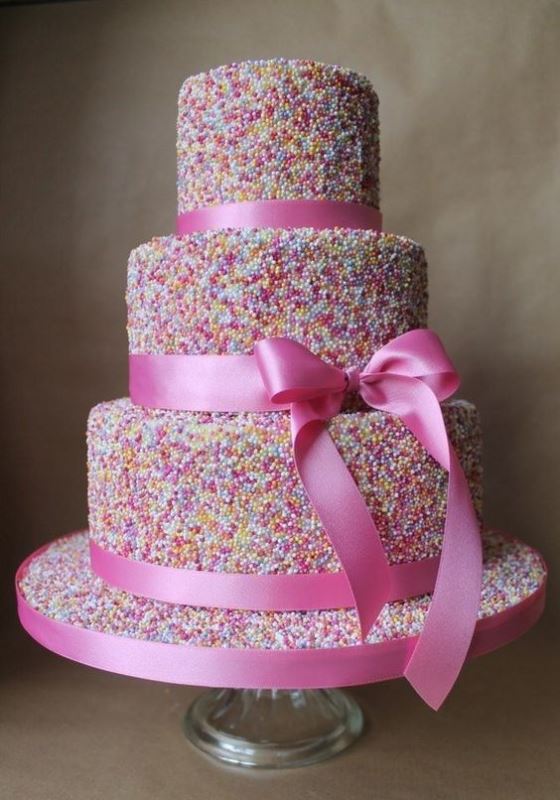 a three-tier wedding cake fully covered with sprinkles and with pink ribbons is a bold and whimsy idea to rock