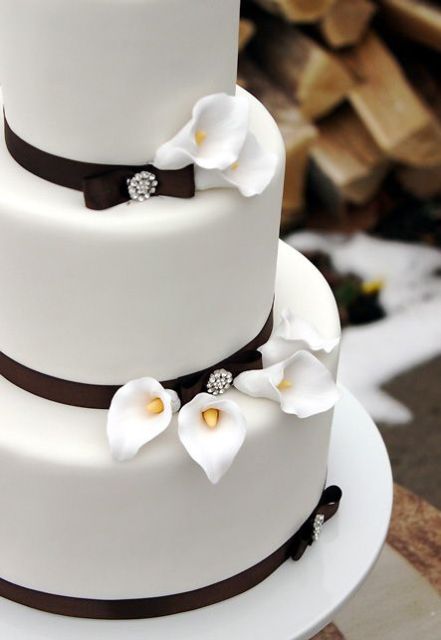a white wedding cake with brown ribbons and brooches plus white calla lilies is an elegant and chic idea