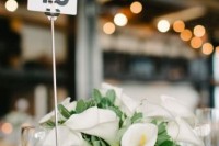 a wedding centerpiece of white calla lilies, greenery and a table number is a cool and chic idea for a wedding