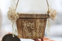 a wooden bucket decorated with fabric blooms, ribbons and calligraphy for a rustic wedding