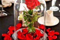 a cloche with a single red rose and petal around is a chic and bright Disney themed wedding centerpiece