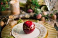 a chic place setting with a gold charger with moss on it, a red apple with calligraphy for a Snow White hint
