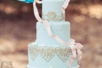 an aqua wedding cake with gold lace and little birdies with a ribbon like in Disney’s cartoons