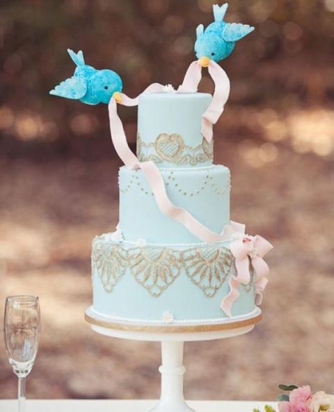 an aqua wedding cake with gold lace and little birdies with a ribbon like in Disney's cartoons