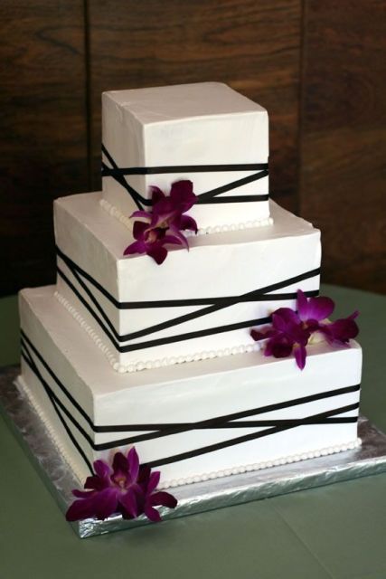 a white square wedding cake wth black ribbons and purple orchids for a tropical wedding