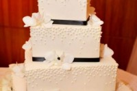 a textural white square wedding cake decorated with black ribbons and white blooms