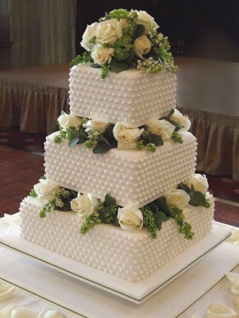 a white square wedding cake with beading and fresh white blooms plus greenery