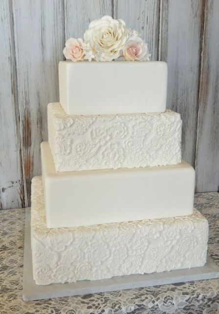 A white square wedding cake with patterned and sleek tiers and neutral fresh blooms on top