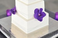 a white square wedding cake with bright purple blooms for a colorful accents