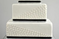 a white wedding cake with white edible beads and black ribbons, rhinestones and a large sugar bloom on top