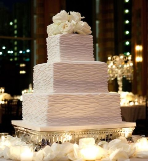 a patterned white wedding cake topped with white roses for a formal wedding