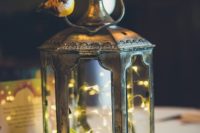 Tinkerbell’s Hideaway wedding centerpiece of a metal lantern with LEDs, moss, a little nest and a birdie on it