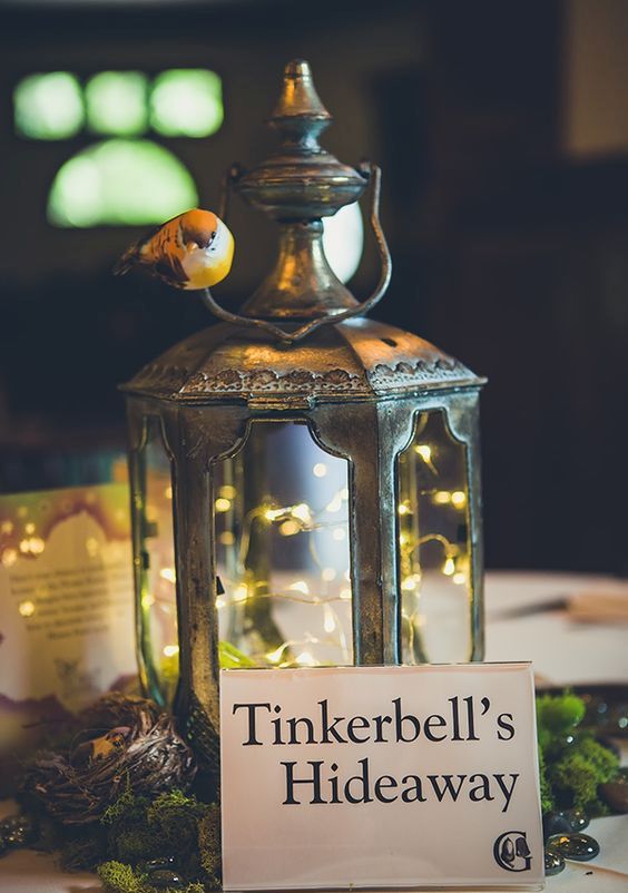 Tinkerbell's Hideaway wedding centerpiece of a metal lantern with LEDs, moss, a little nest and a birdie on it