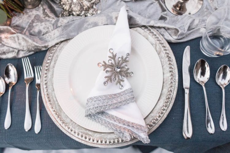 a Frozen inspired place setting with a silver charger, a lace trim napkin plus a rhinestone snowflake as a napkin ring