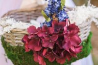 a basket decorated with moss, blue and burgundy blooms is a cool idea for a flower girl
