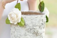 a basket made of tree bark and decorated with fabric blooms and greenery is a nice fit for a rustic wedding