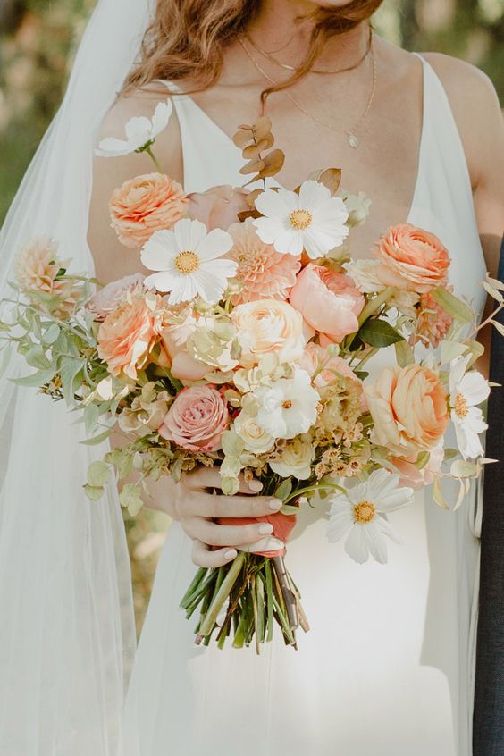 a beautiful textural wedding bouquet of orange and pink roses and ranunculus, white blooms and greenery plus dried foliage