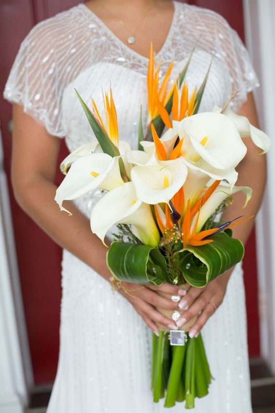a bold tropical wedding bouquet of white calla lilies and orange blooms plus a wrap with a photo is amazing