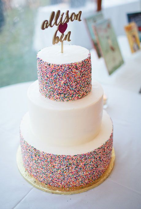 a bold wedding cake with a white and colorful sprinkle tiers, a gold calligraphy and heart topper for much fun