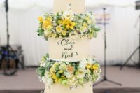 a bright summer wedding cake with floral tiers and white and yellow blooms and greenery between the tiers