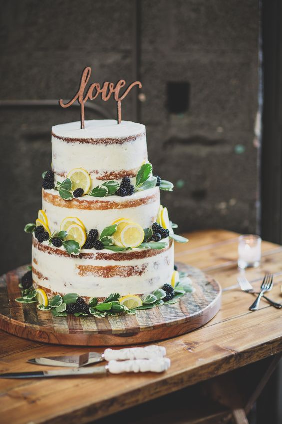 a chic naked wedding cake with fresh citrus slices, blackberries and greenery plus a calligraphy topper