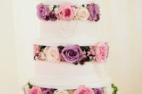 a chic wedding cake with pink, purple and blush blooms and pearls between the tiers