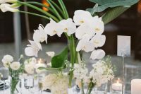 a cluster wedding centerpiece of clear glasses with white callas, orchids, ranunculus and other blooms, all white and chic