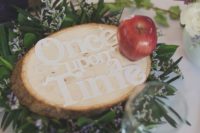 a cool Disney-themed wedding centerpiece with fresh blooms and greenery, a wooden slice with letters and a single apple
