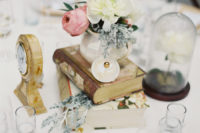 a creative Disney wedding centerpiece with vintage books, a clock, a cloche with a flower, a hand mirror and blooms