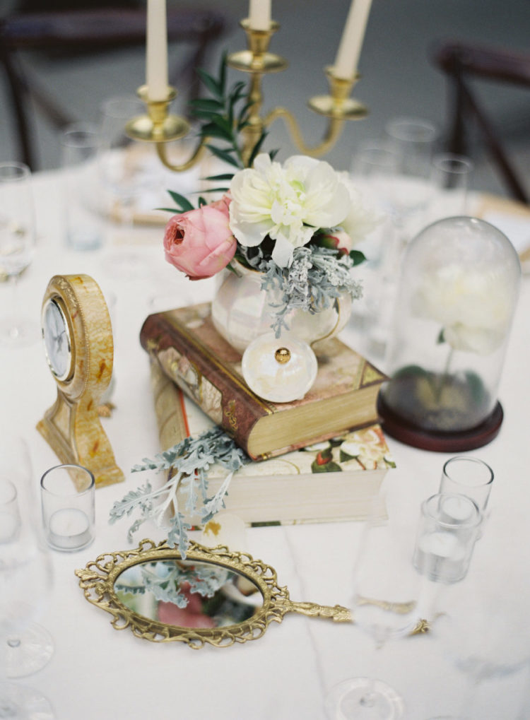 a creative Disney wedding centerpiece with vintage books, a clock, a cloche with a flower, a hand mirror and blooms