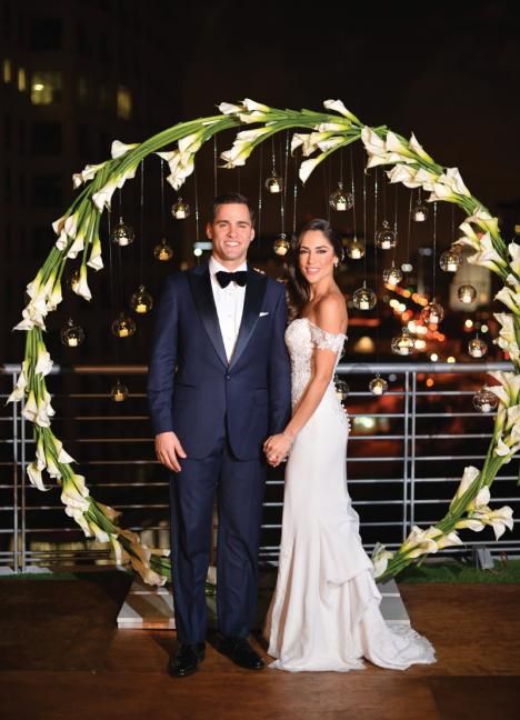 a creative round wedding arch covered with white callas and with hanging candle spheres is a refined and chic idea