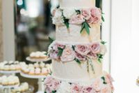 a cute wedding cake with white patterned tiers, lilac and white blooms between the tiers is veyr softening
