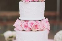 a cute white patterned wedding cake with pink roses between the tiers looks super cool