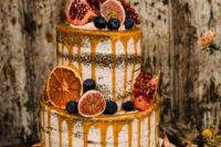 a decadent fall semi naked wedding cake decotated with fresh berries, figs, pomegranates, candied citrus and caramel drip