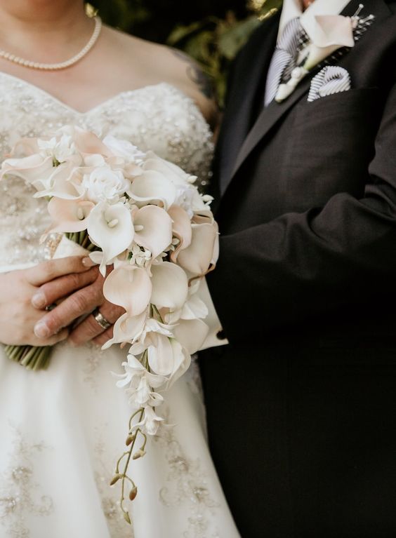 a delicate cascading wedding bouquet of white and blush callas and small roses is a very chic idea for a refined bride, great for spring or summer