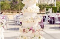 a glam wedding cake with white patterned tiers, white and blush blooms, very lush and chic