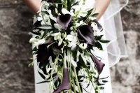 a gorgeous cascading wedding bouquet of deep purple callas and white blooms, greenery and twigs for a mmoody wedding