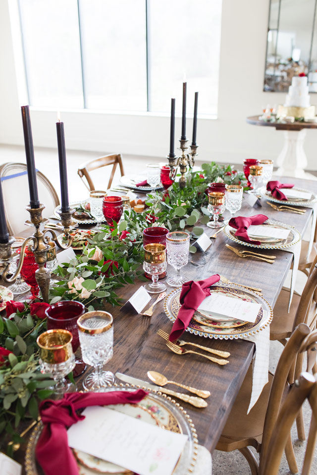 a gorgeous the Beauty and the Beast wedding tablescape with greenery and bright blooms, burgundy napkins, black candles and touches of gold