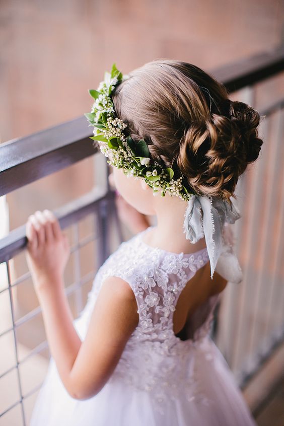 a half updo with a braided halo, a braided and wavy top knot, a bump and a greenerycrown with a white bow