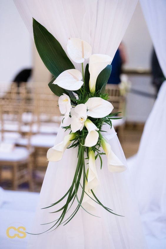 a lovely wedding decoration - a white curtain accented with white callas and orchids plus large leaves is a pretty idea