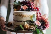 a lush fall wedding cake topped with grapes, figs, dark blooms, leaves and other stuff and gold leaf