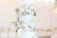 a luxurious white wedding cake with white orchids, lilac and blush blooms between the tiers
