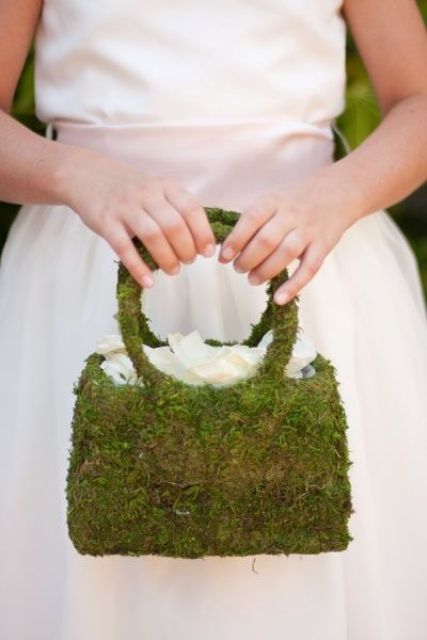 a moss purse-shaped flower girl basket with white petals is a unique idea for a wedding